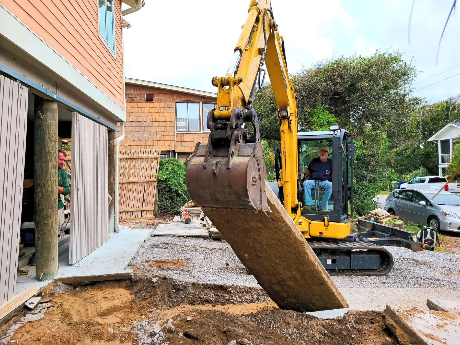 Excavator grading and moving soil beneath a raised home during a site work project