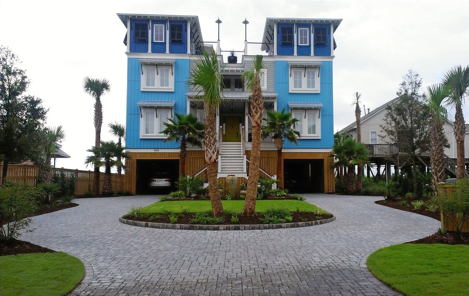 Circular paver driveway, palms and manicured lawn at a blue raised coastal home in the Charleston area
