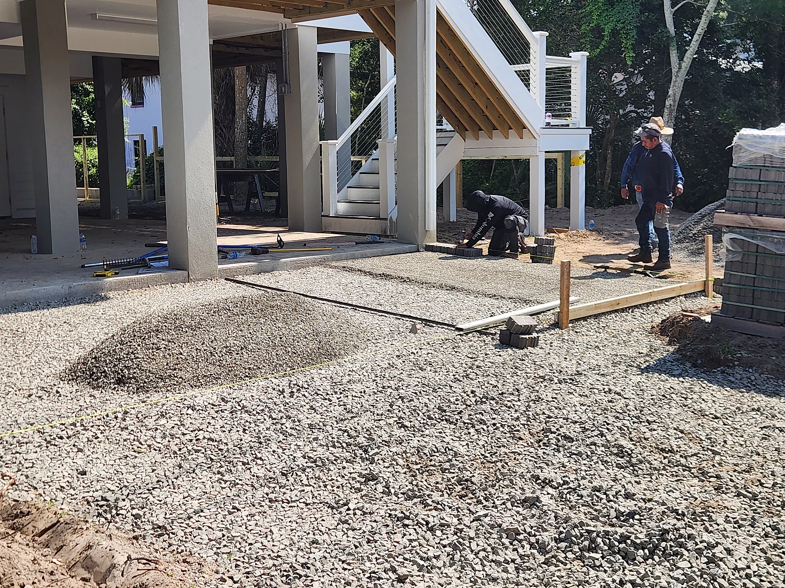 Crew spreading and compacting a gravel base beneath an elevated Lowcountry home