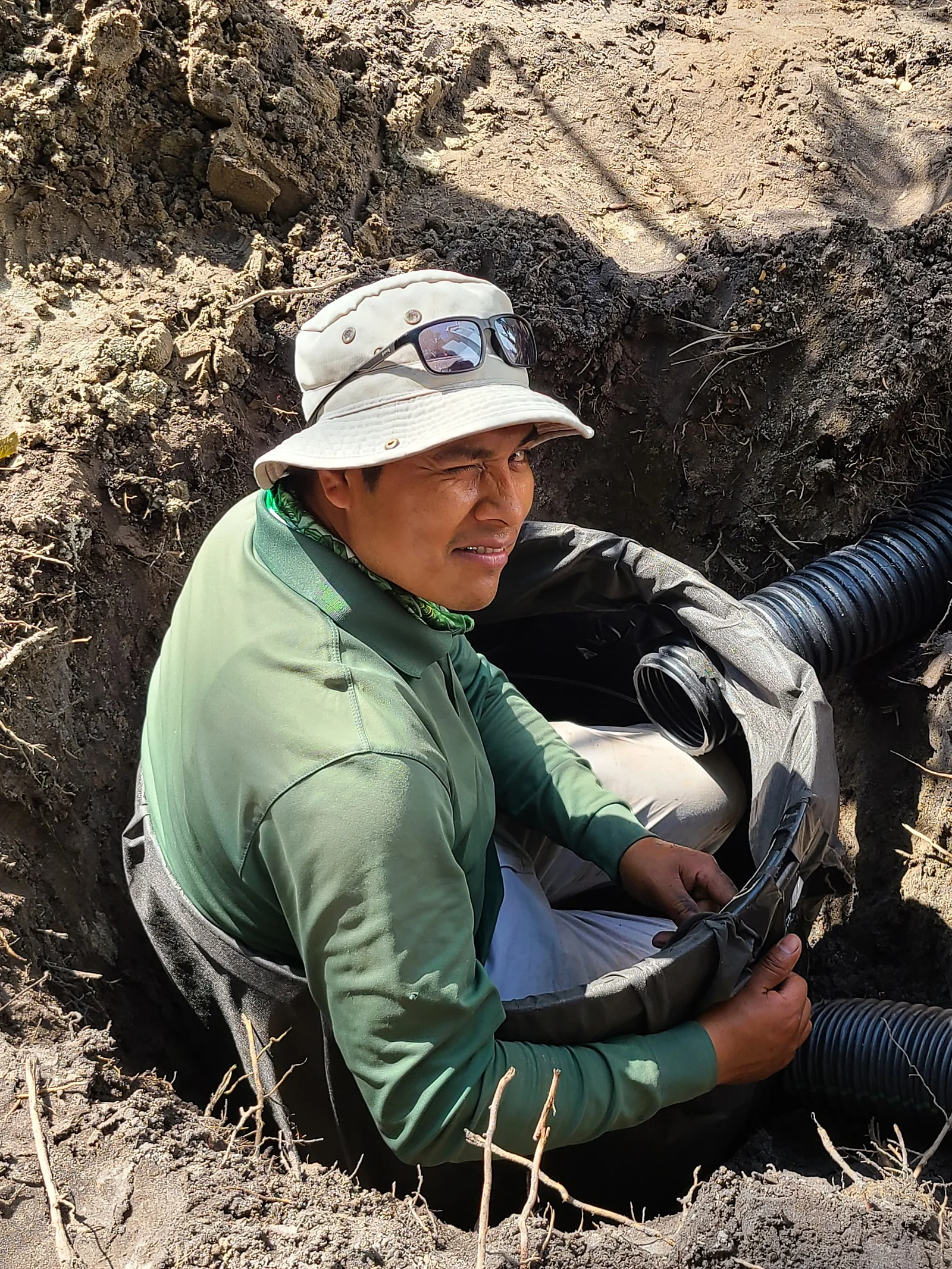 Crew member fitting corrugated drainage pipe in a hand-dug trench