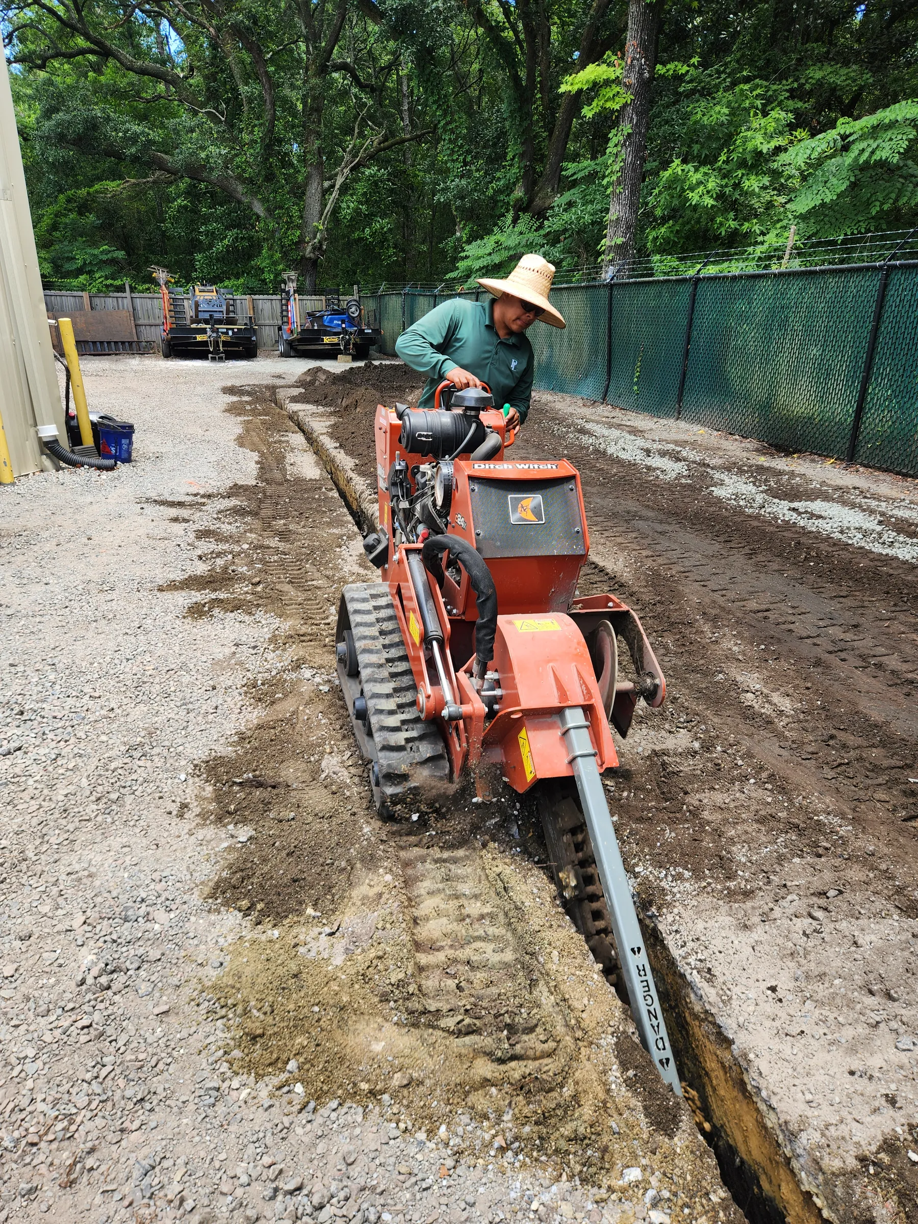 Compact excavator trenching alongside a foundation for drainage and irrigation work