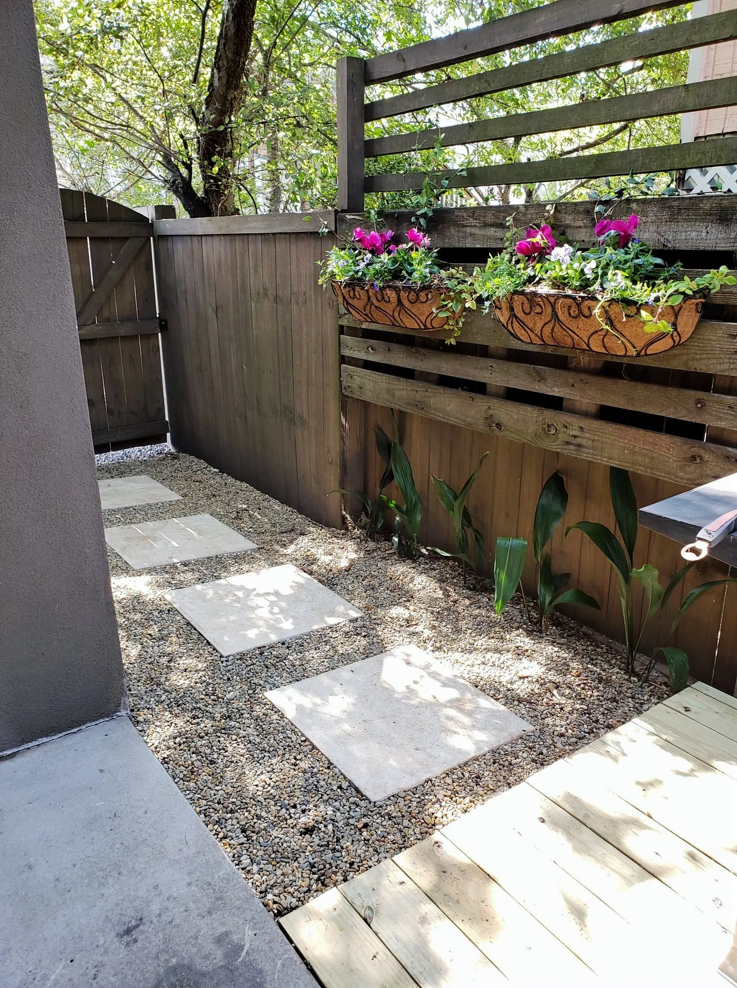 Raised wooden planter boxes with seasonal flowers beside a gravel and paver patio